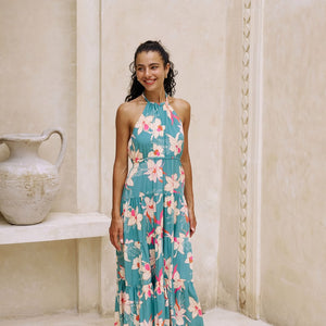 woman with brown hair wearing tiered halter maxi dress in teal with large cream colored orchids.
