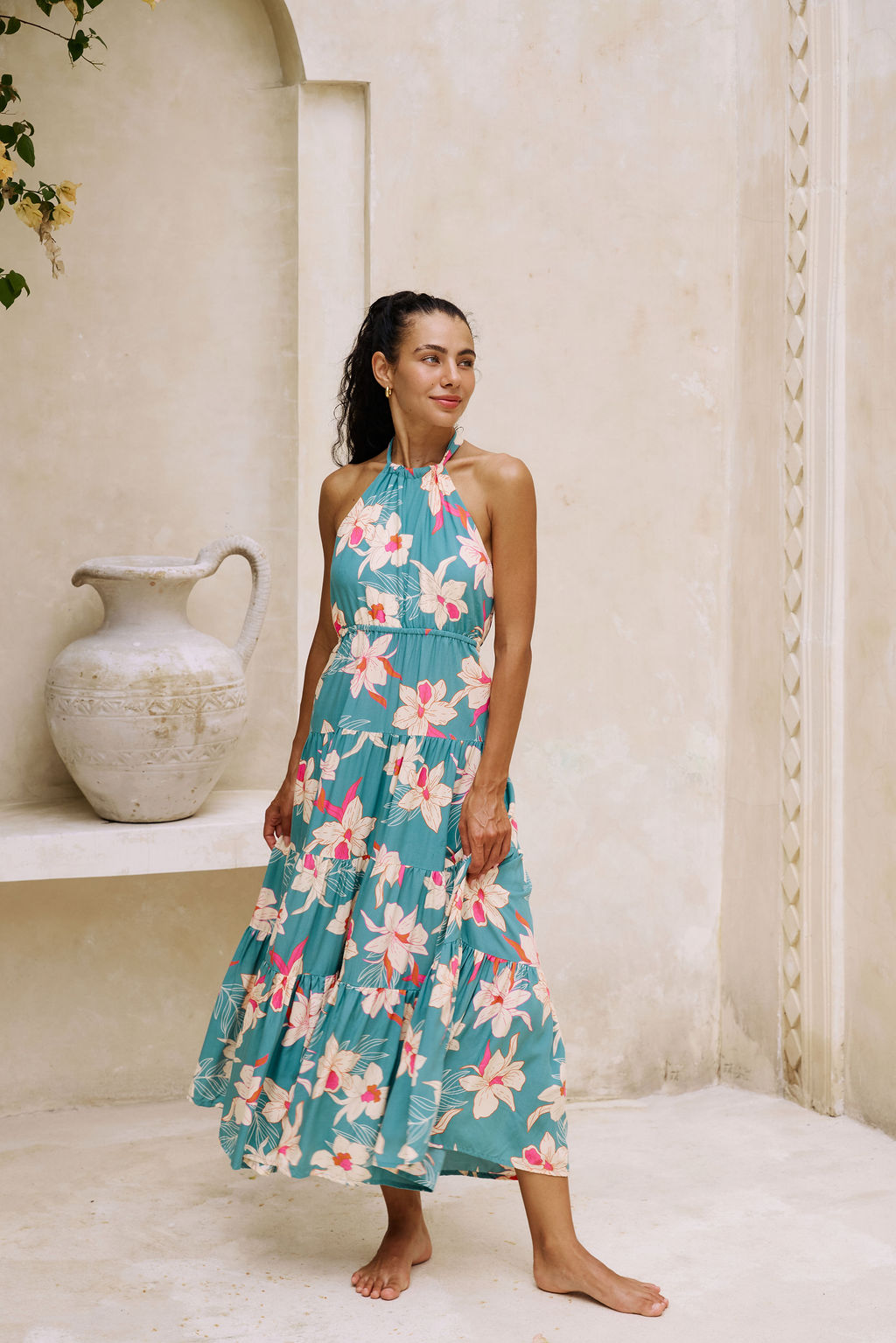 woman with brown hair wearing tiered halter maxi dress in teal with large cream colored orchids.