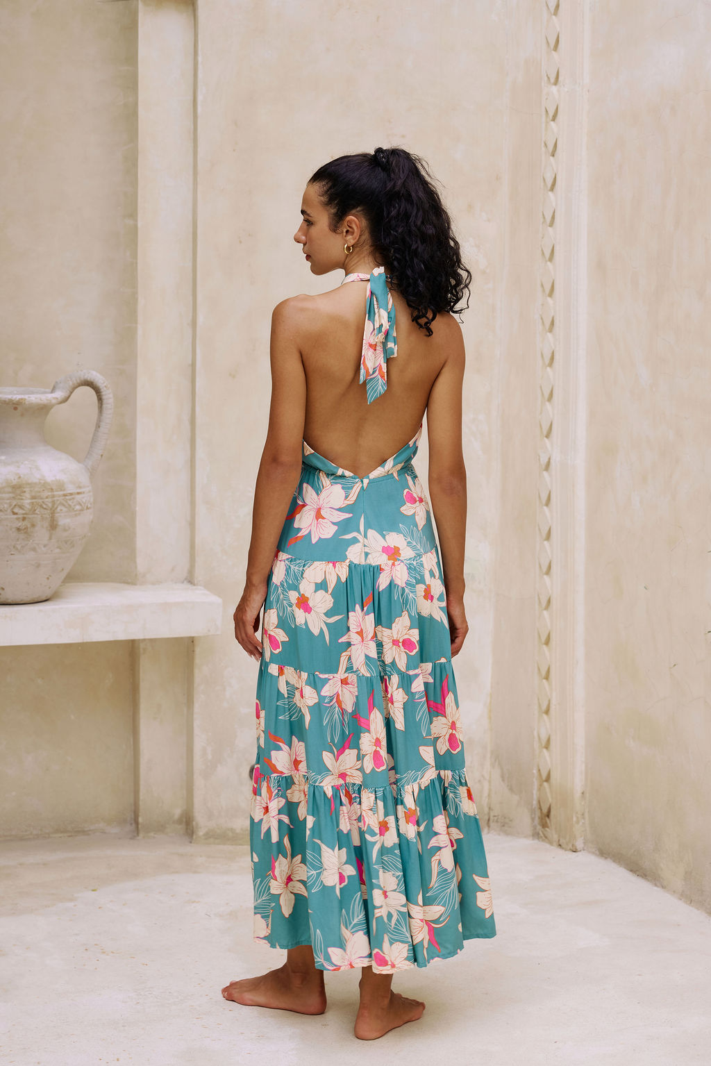 woman with brown hair wearing tiered halter maxi dress in teal with large cream colored orchids.