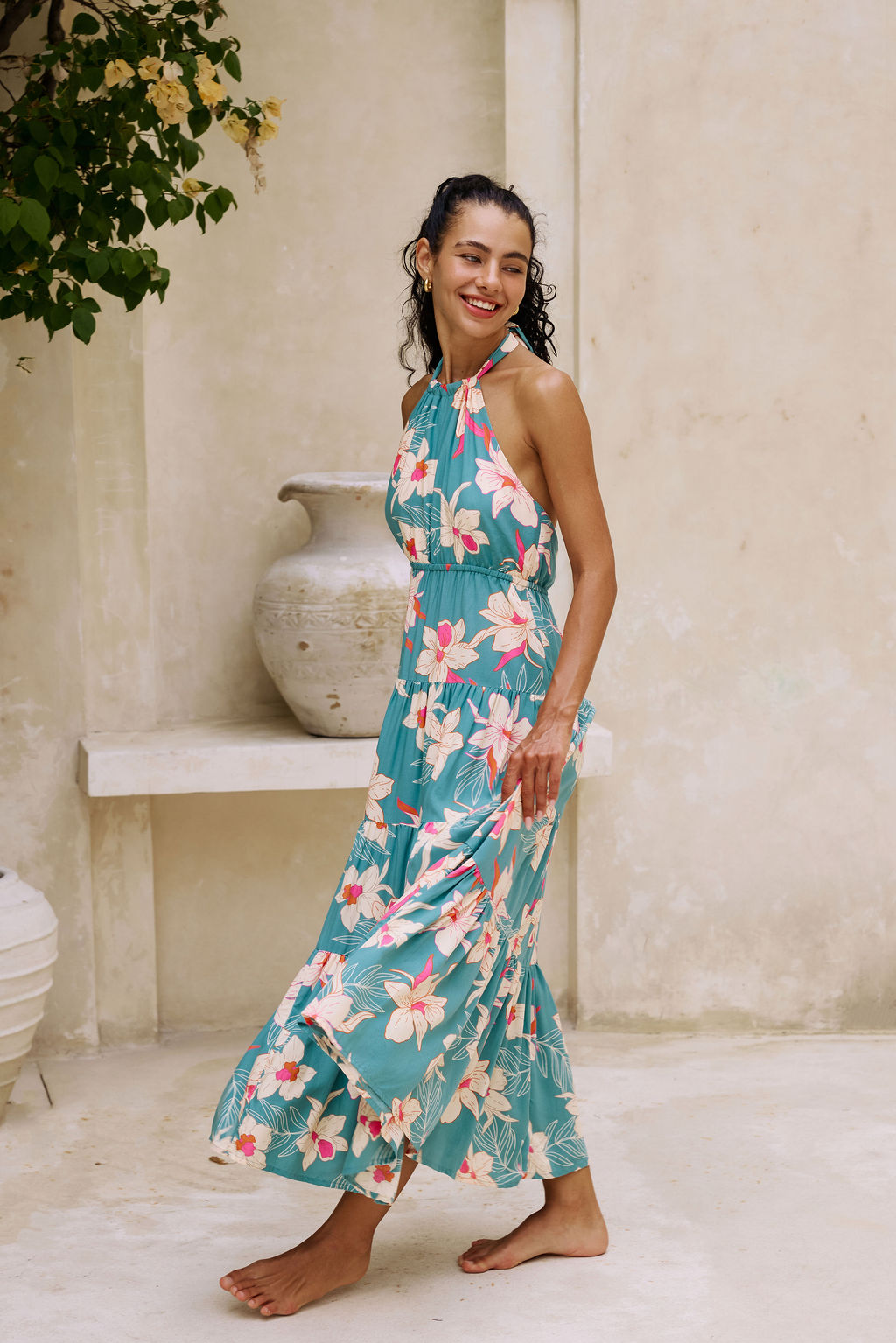 woman with brown hair wearing tiered halter maxi dress in teal with large cream colored orchids.