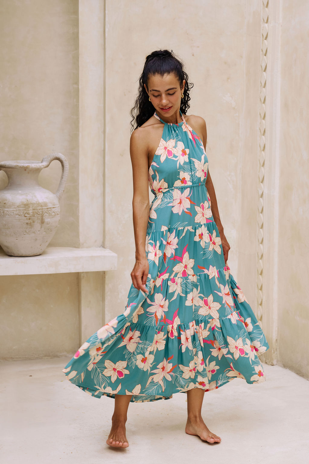 woman with brown hair wearing tiered halter maxi dress in teal with large cream colored orchids.