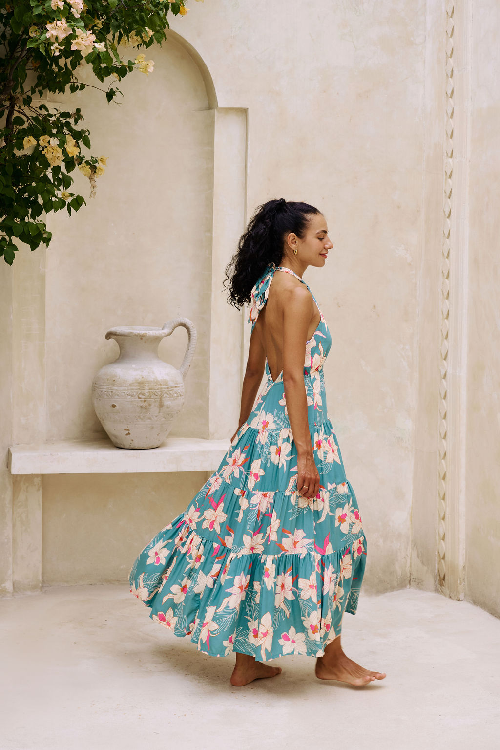 woman with brown hair wearing tiered halter maxi dress in teal with large cream colored orchids.