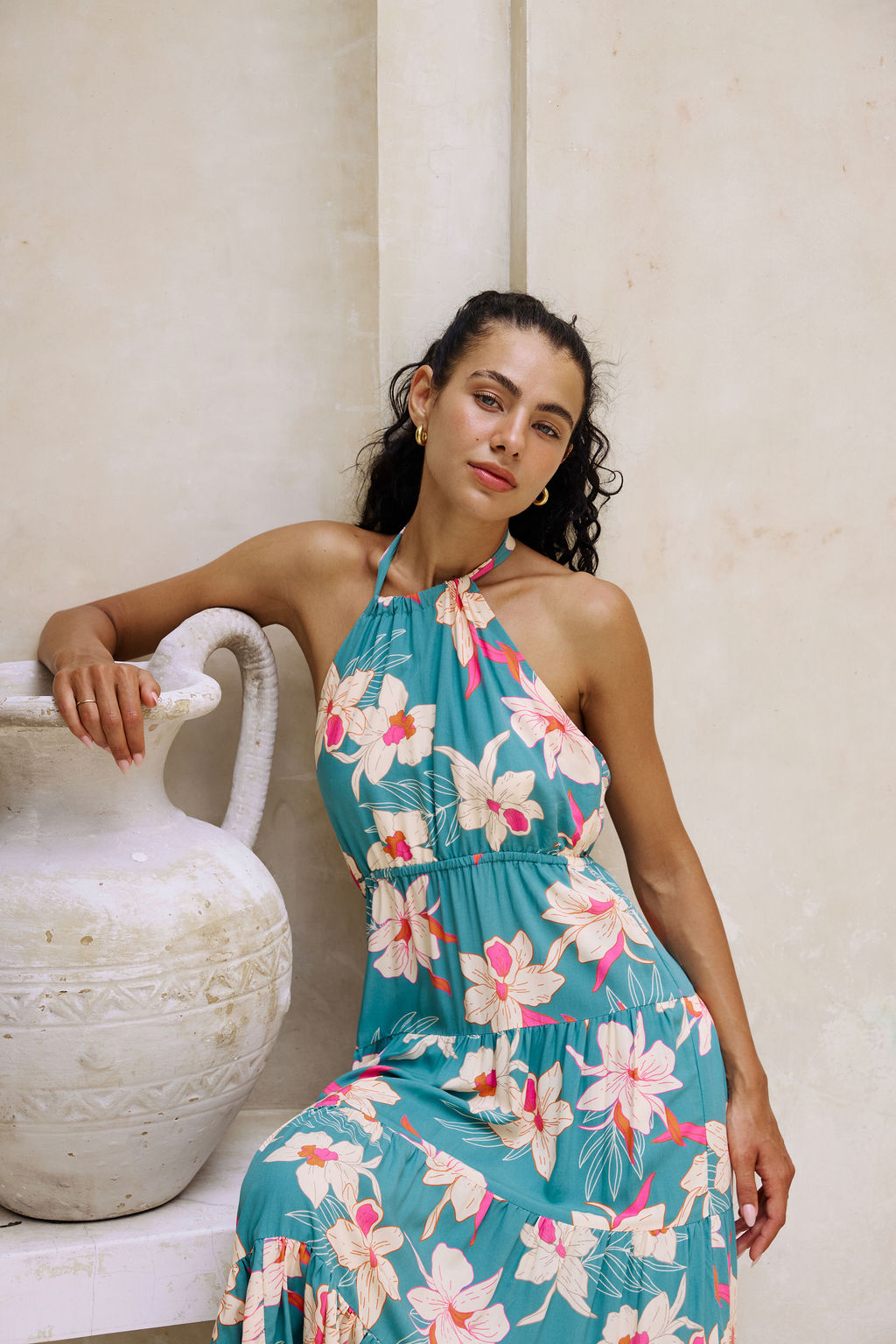 woman with brown hair wearing tiered halter maxi dress in teal with large cream colored orchids.