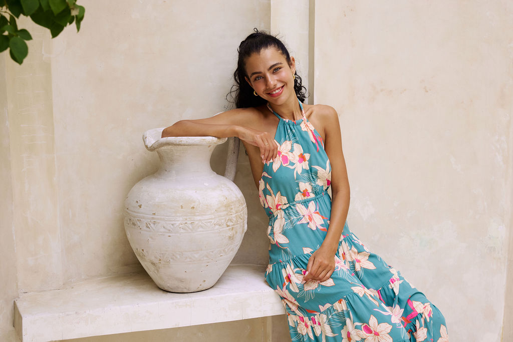 woman with brown hair wearing tiered halter maxi dress in teal with large cream colored orchids.