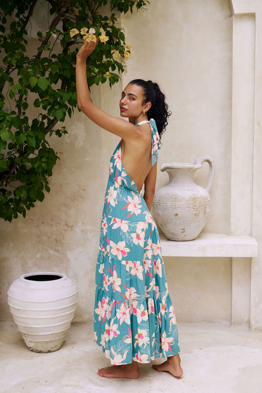 woman with brown hair wearing tiered halter maxi dress in teal with large cream colored orchids.