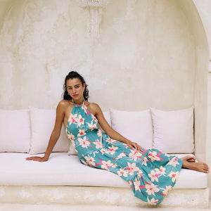 woman with brown hair wearing tiered halter maxi dress in teal with large cream colored orchids.