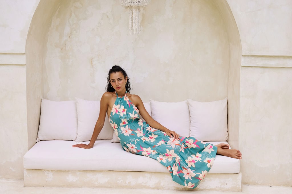 woman with brown hair wearing tiered halter maxi dress in teal with large cream colored orchids.