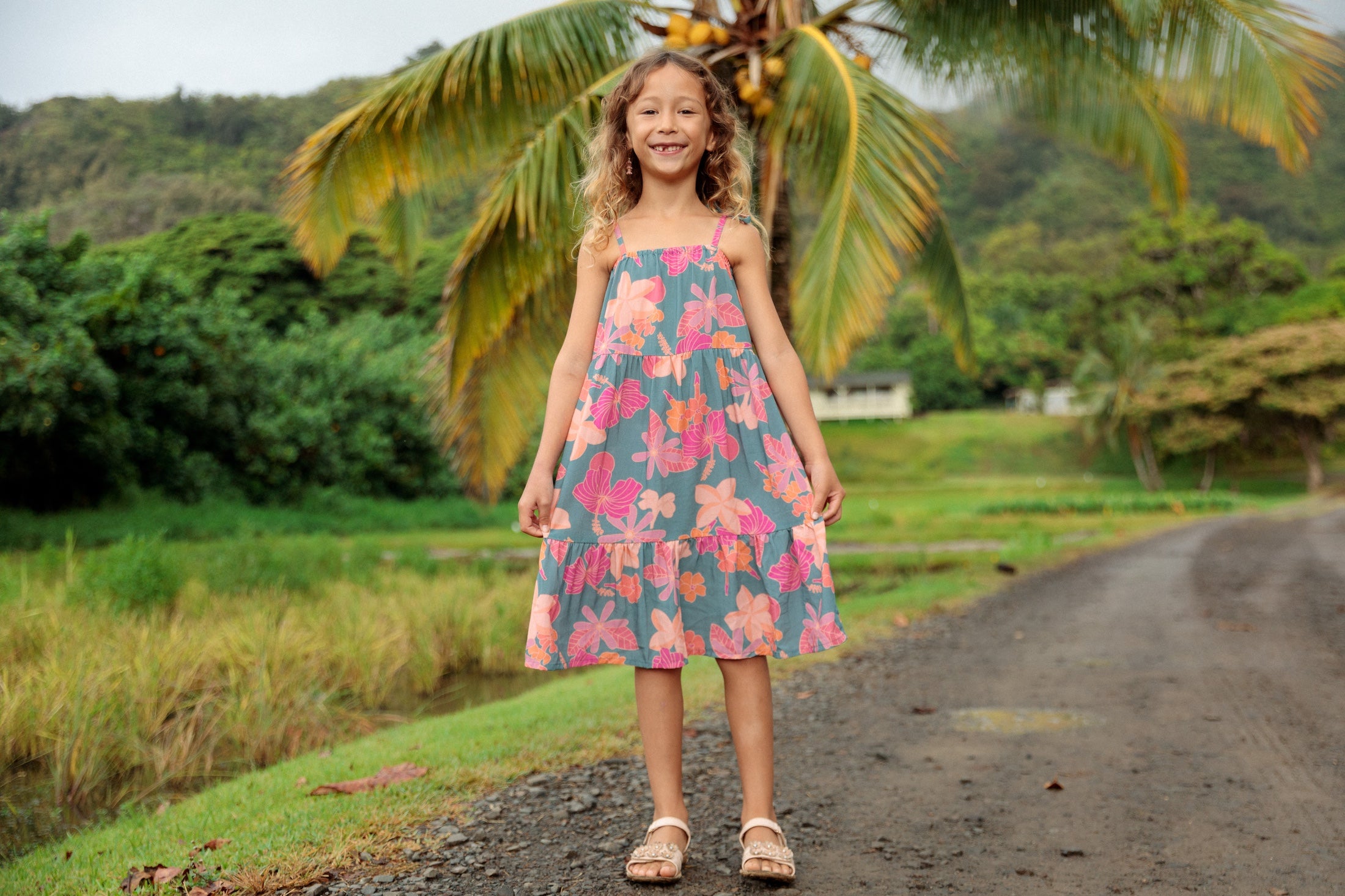 little girl wearing long teal dress with tie sleeve and floral pattern