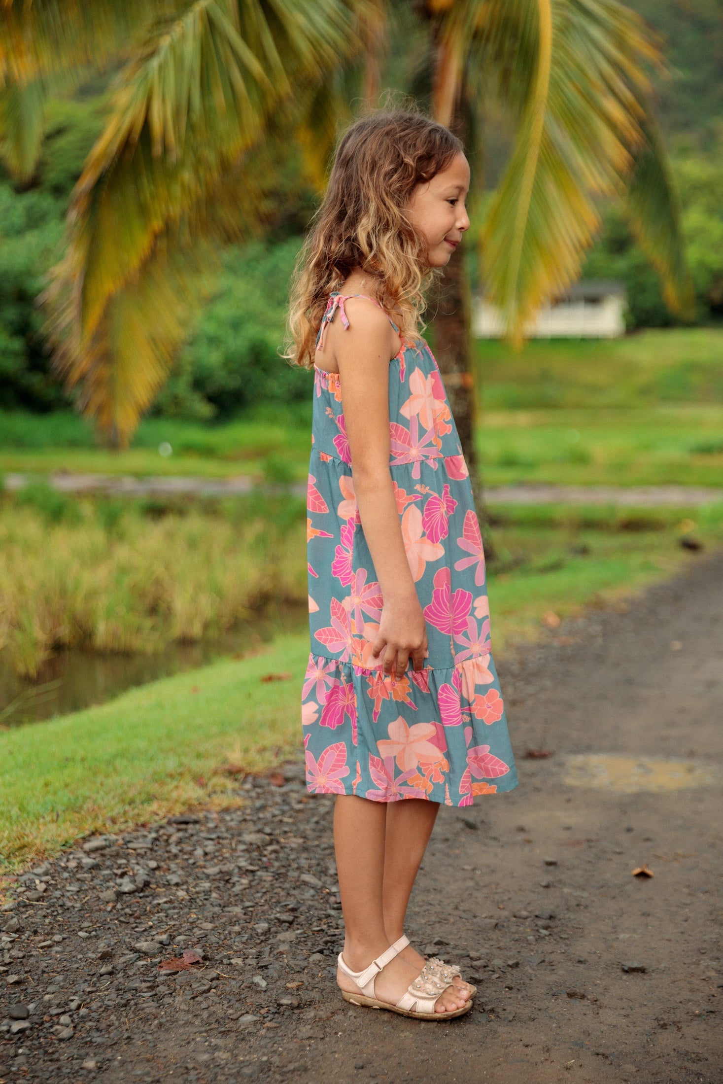 little girl wearing long teal dress with tie sleeve and floral pattern