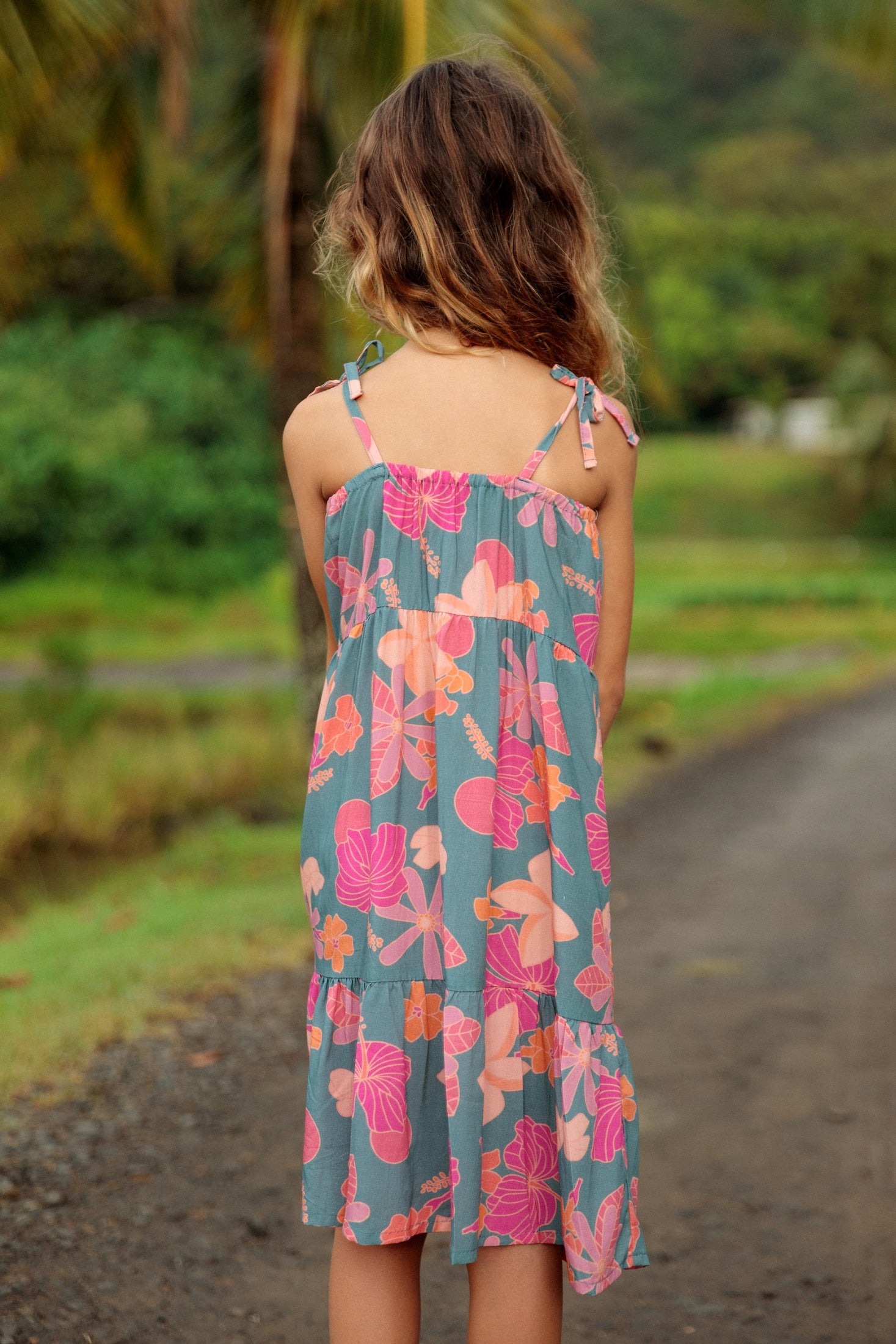 little girl wearing long teal dress with tie sleeve and floral pattern