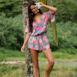woman with brown hair wearing a teal playsuit with orange and pink floral print