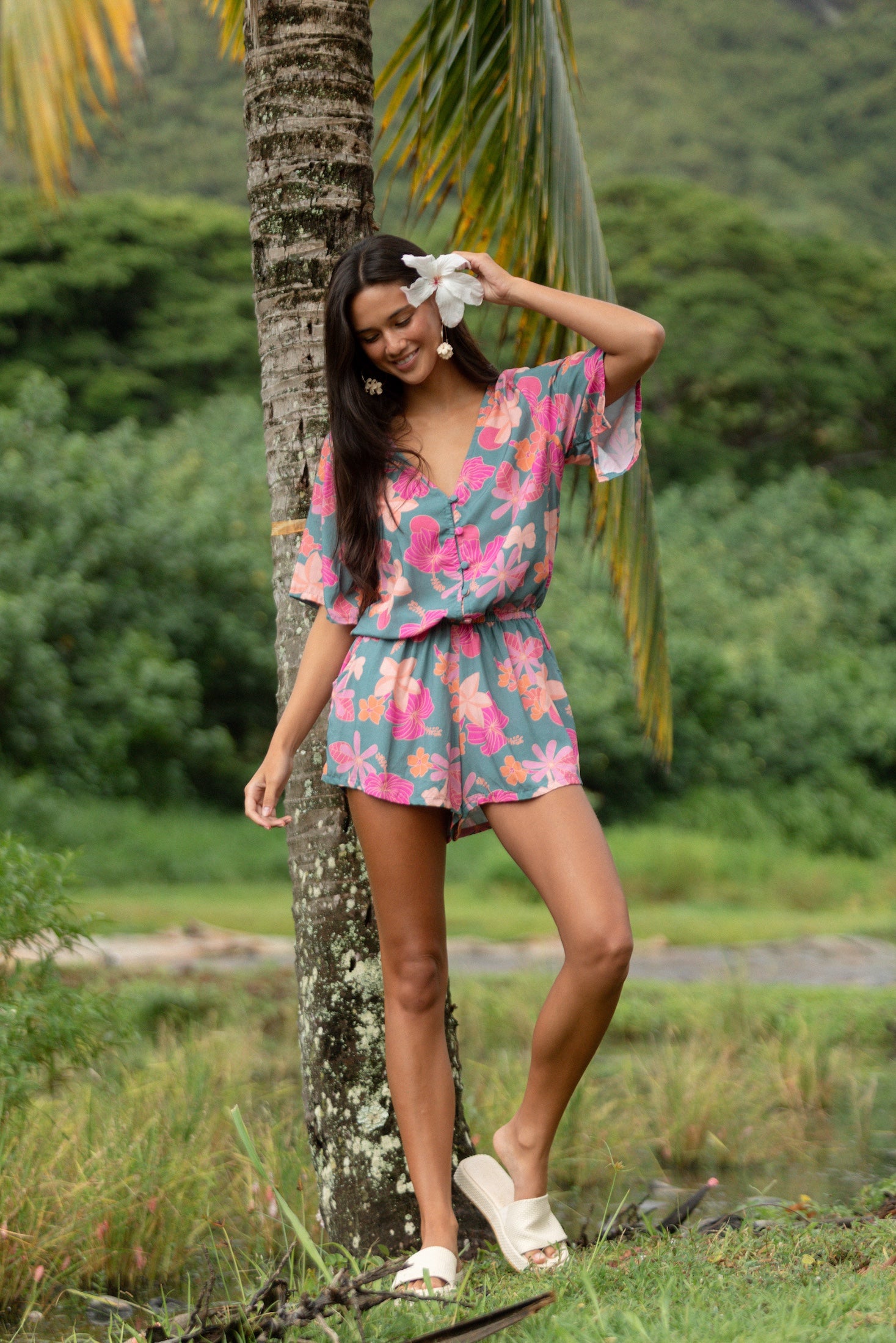 woman with brown hair wearing a teal playsuit with orange and pink floral print