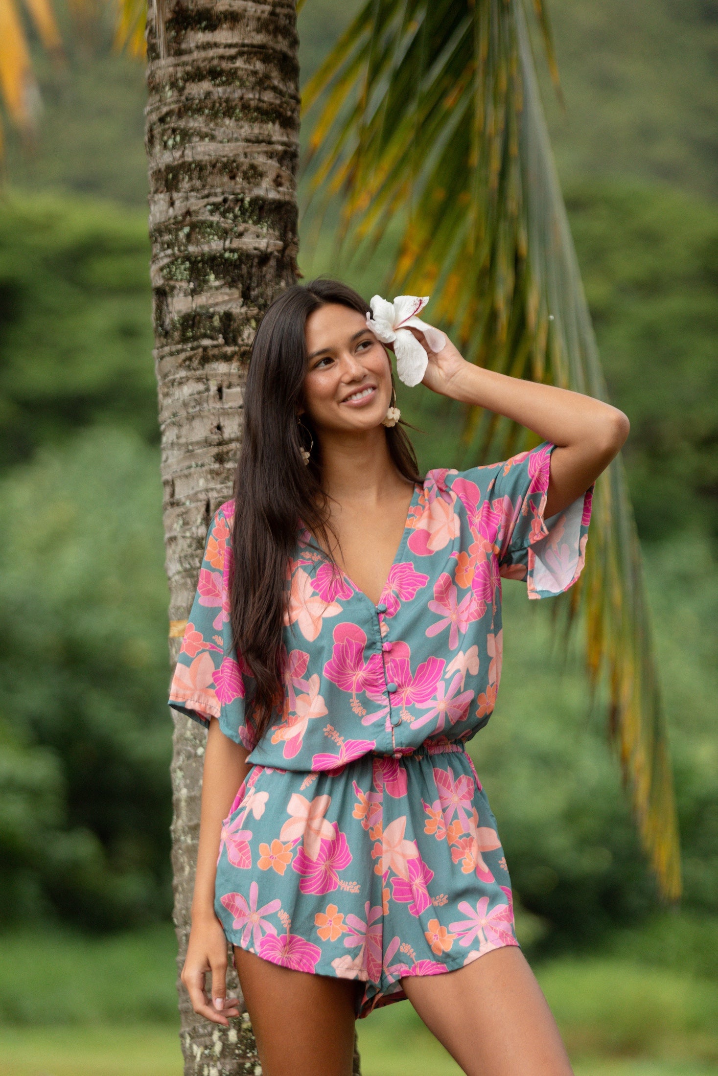 woman with brown hair wearing a teal playsuit with orange and pink floral print