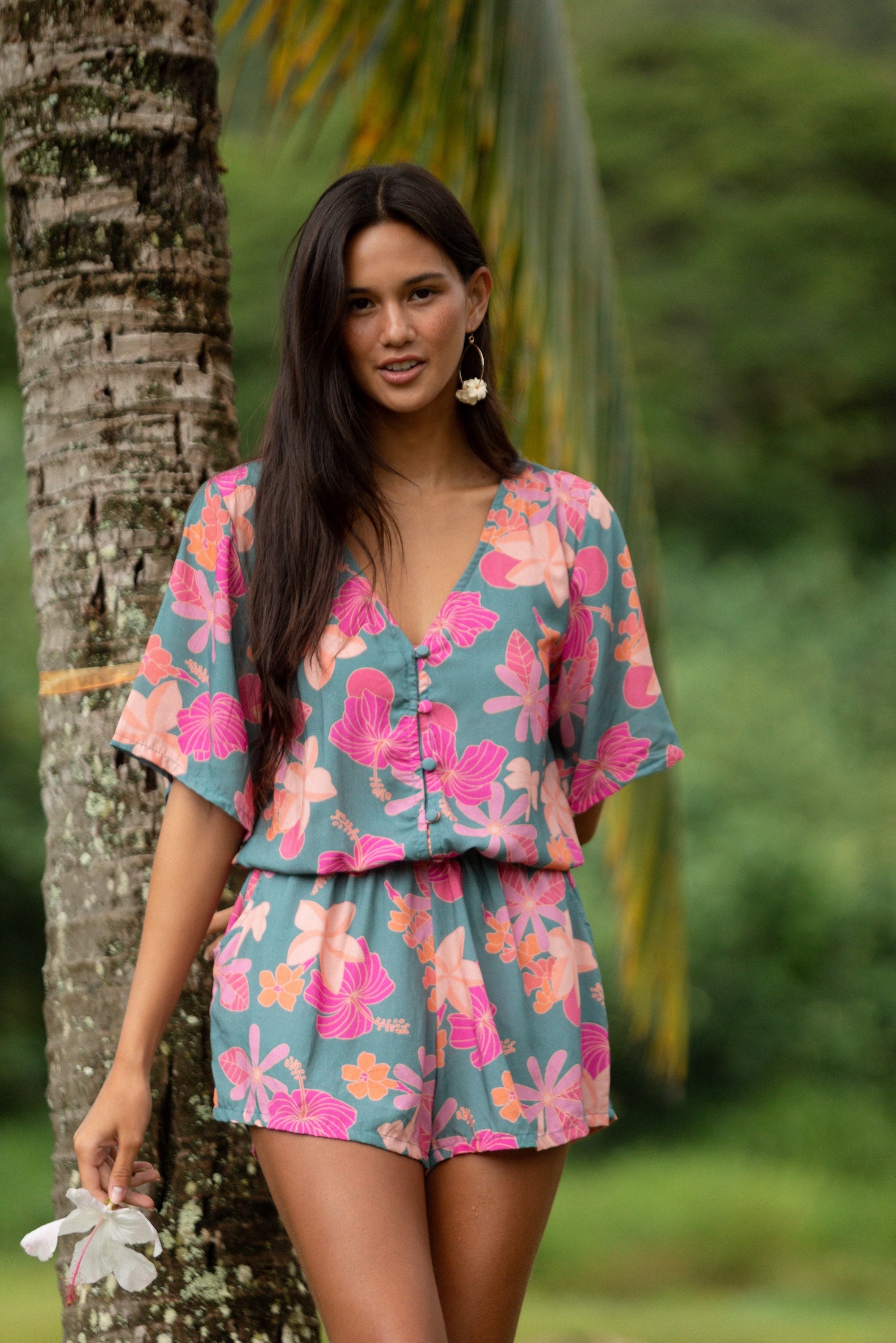 woman with brown hair wearing a teal playsuit with orange and pink floral print