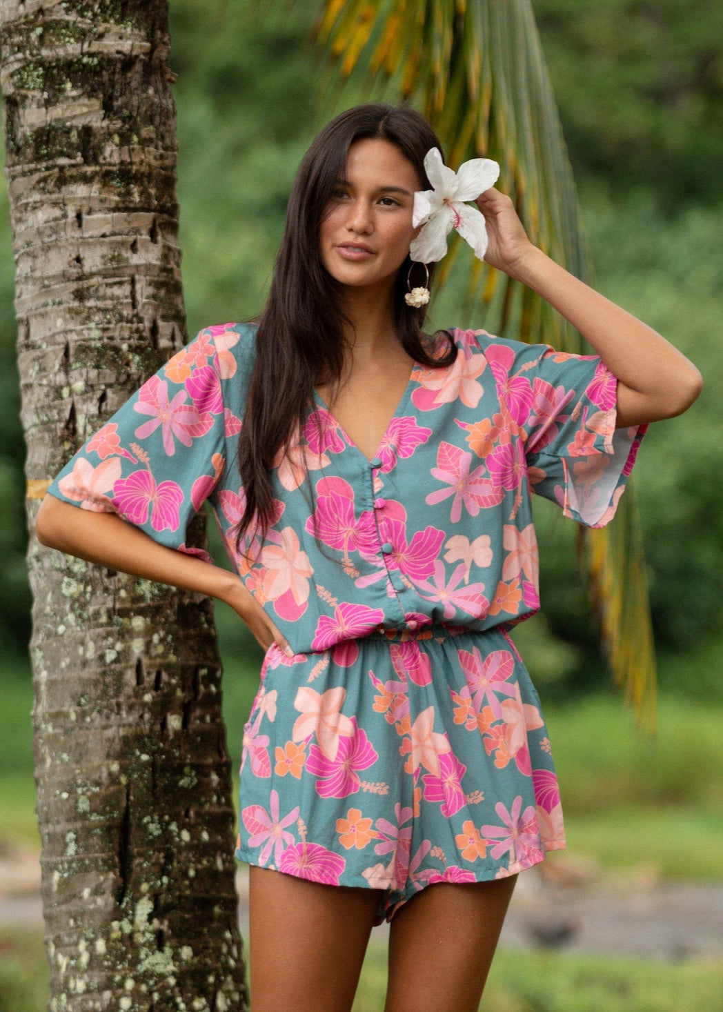 woman with brown hair wearing a teal playsuit with orange and pink floral print