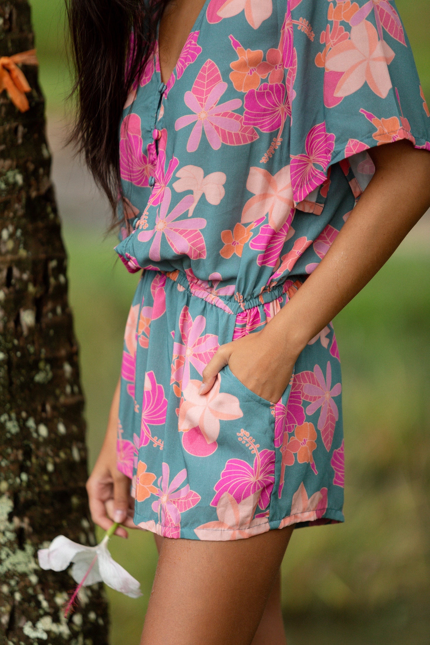 woman with brown hair wearing a teal playsuit with orange and pink floral print