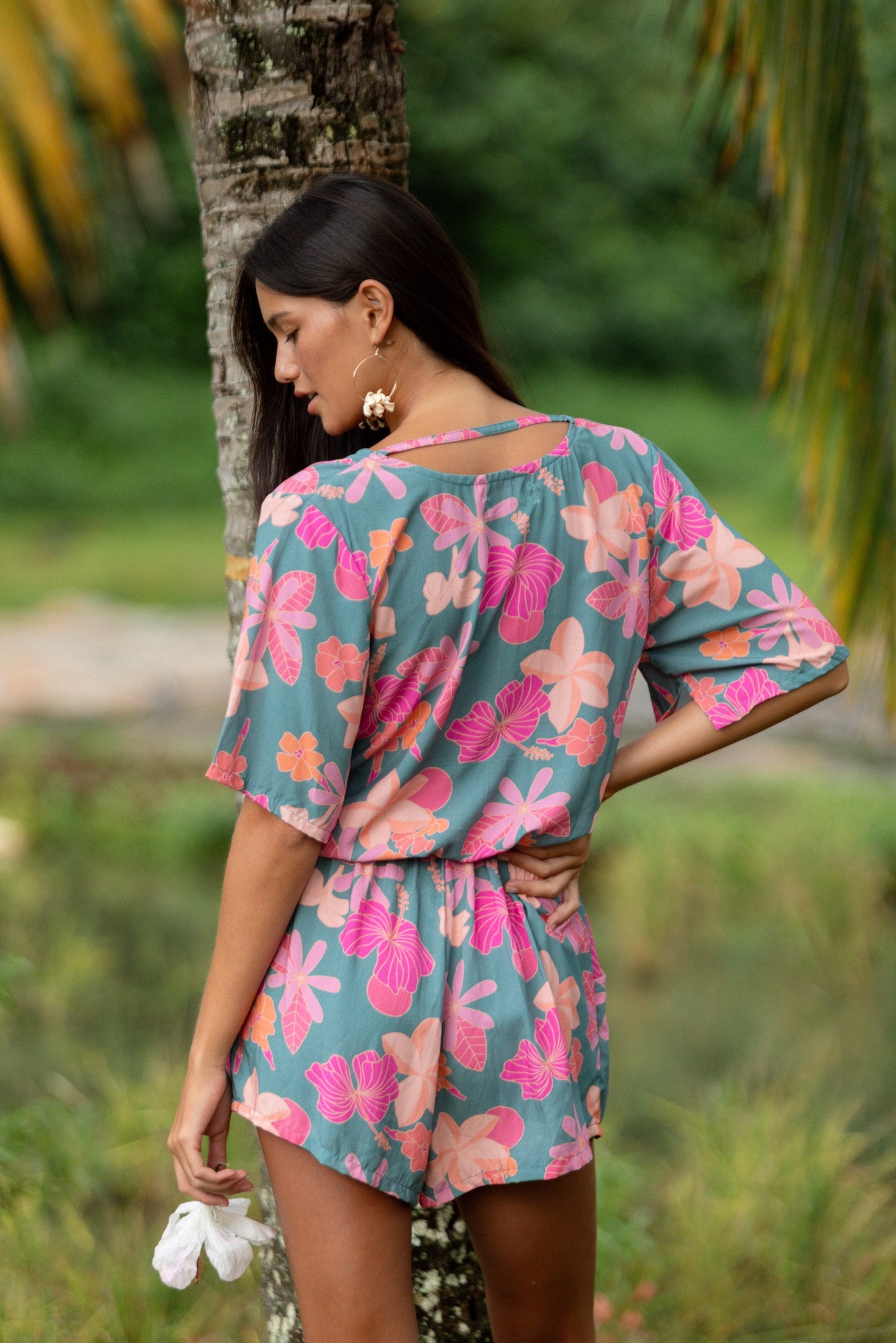 woman with brown hair wearing a teal playsuit with orange and pink floral print