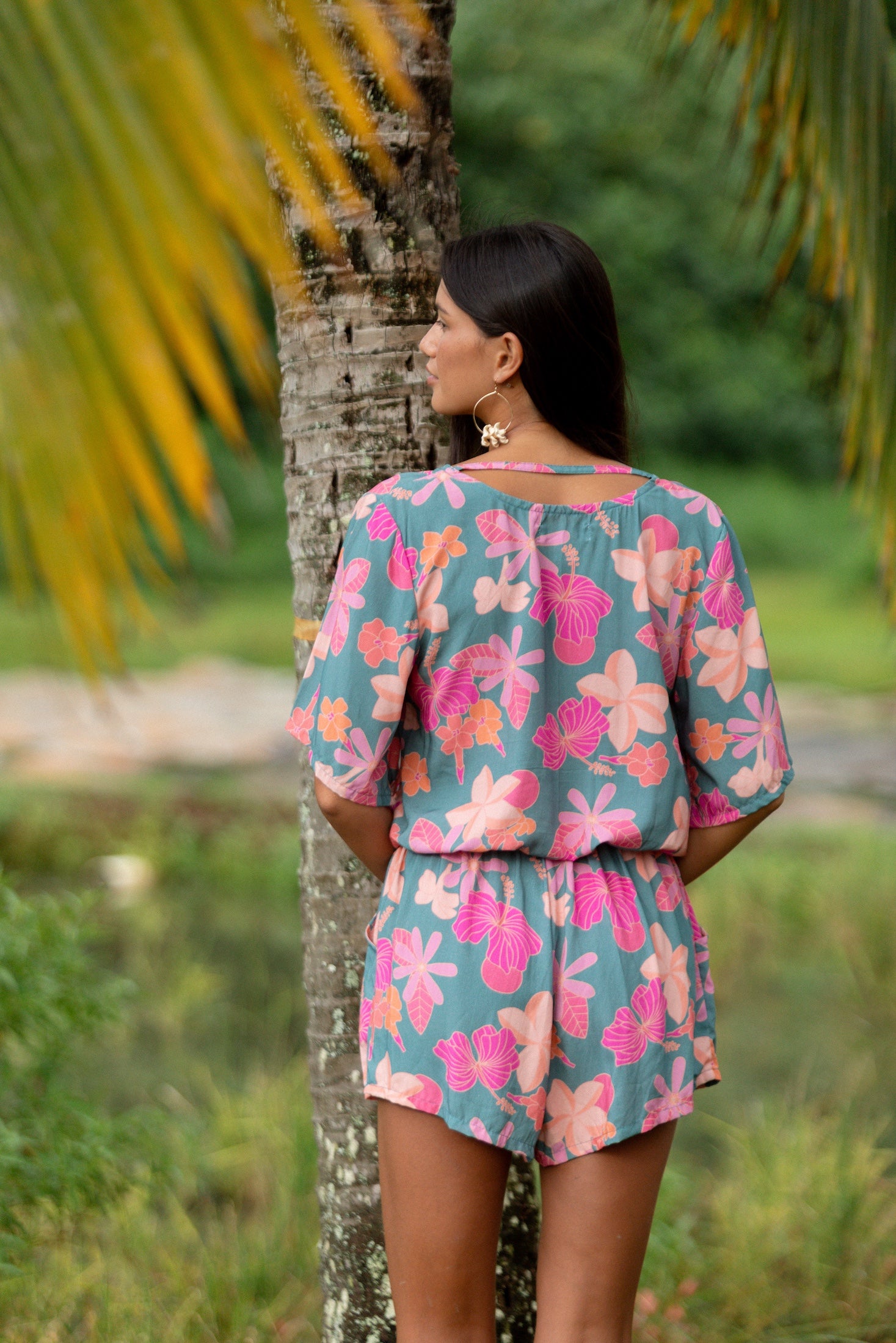 woman with brown hair wearing a teal playsuit with orange and pink floral print