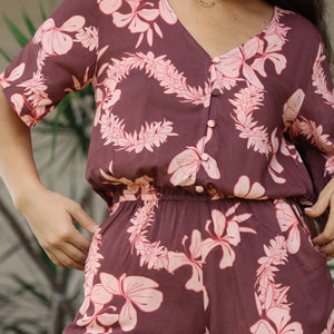 woman with brown hair wearing brown button up playsuit with light pink lei awapuhi print
