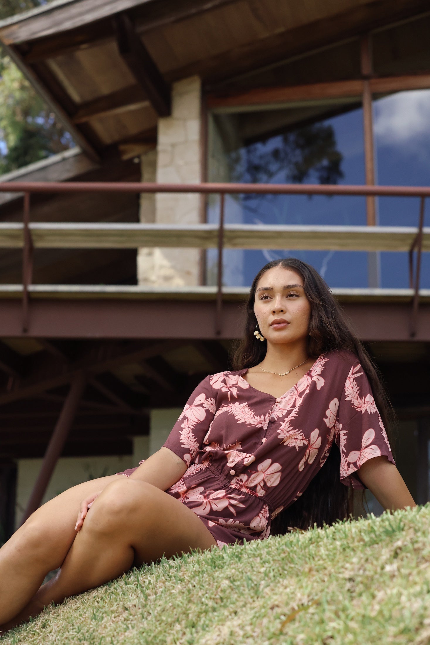 woman with brown hair wearing brown button up playsuit with light pink lei awapuhi print