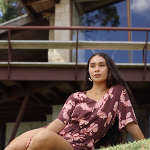 woman with brown hair wearing brown button up playsuit with light pink lei awapuhi print