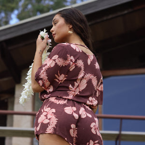 woman with brown hair wearing brown button up playsuit with light pink lei awapuhi print