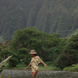 woman with brown hair wearing a short sleeve playsuit in a green color with naupaka pattern throughout.