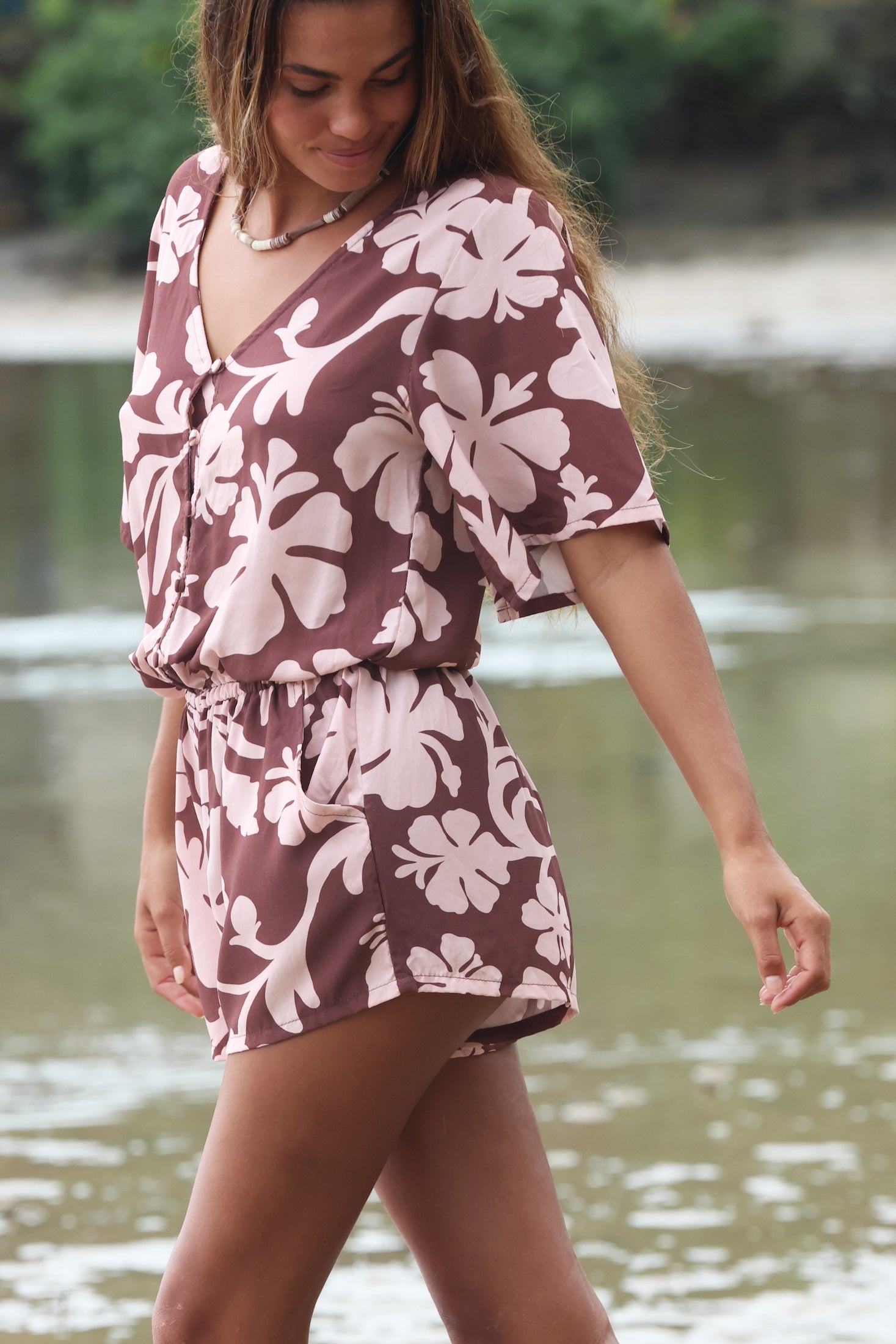 Woman with brown hair wearing a flowy button up playsuit in blush and brown hibiscus print.