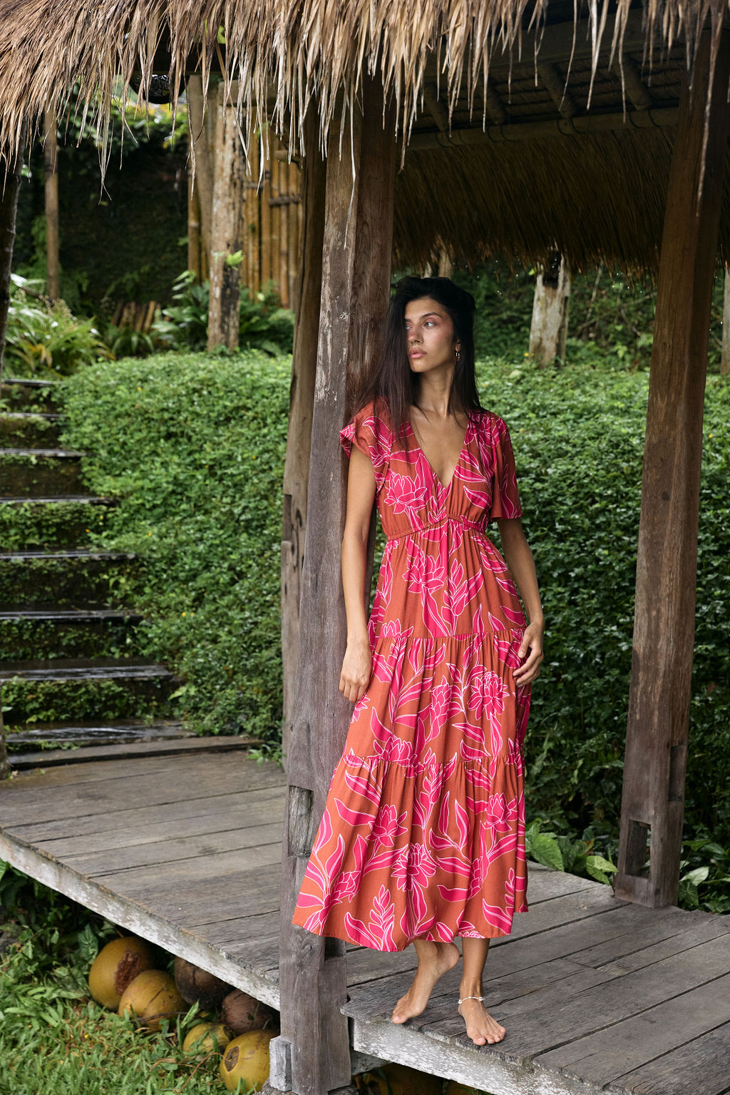 Woman with dark hair wearing tiered maxi dress with sleeves. It is the Mariana Dress in the Garden 'Awapuhi print.