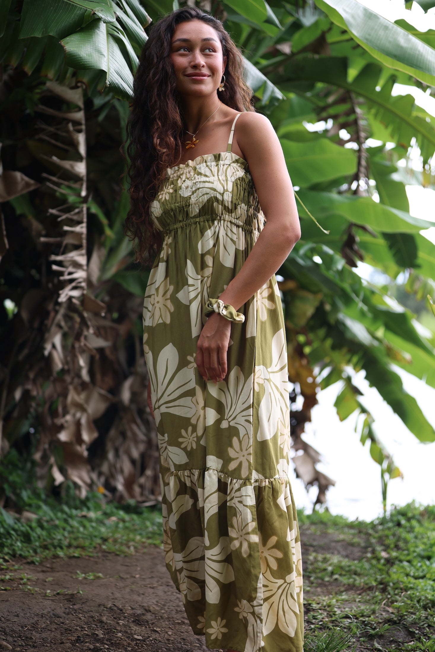 woman with brown hair wearing a maxi flowy dress in a green color with naupaka pattern throughout.
