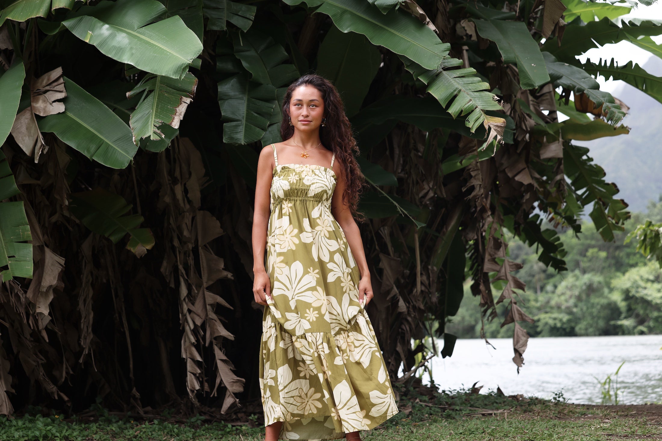 woman with brown hair wearing a maxi flowy dress in a green color with naupaka pattern throughout.