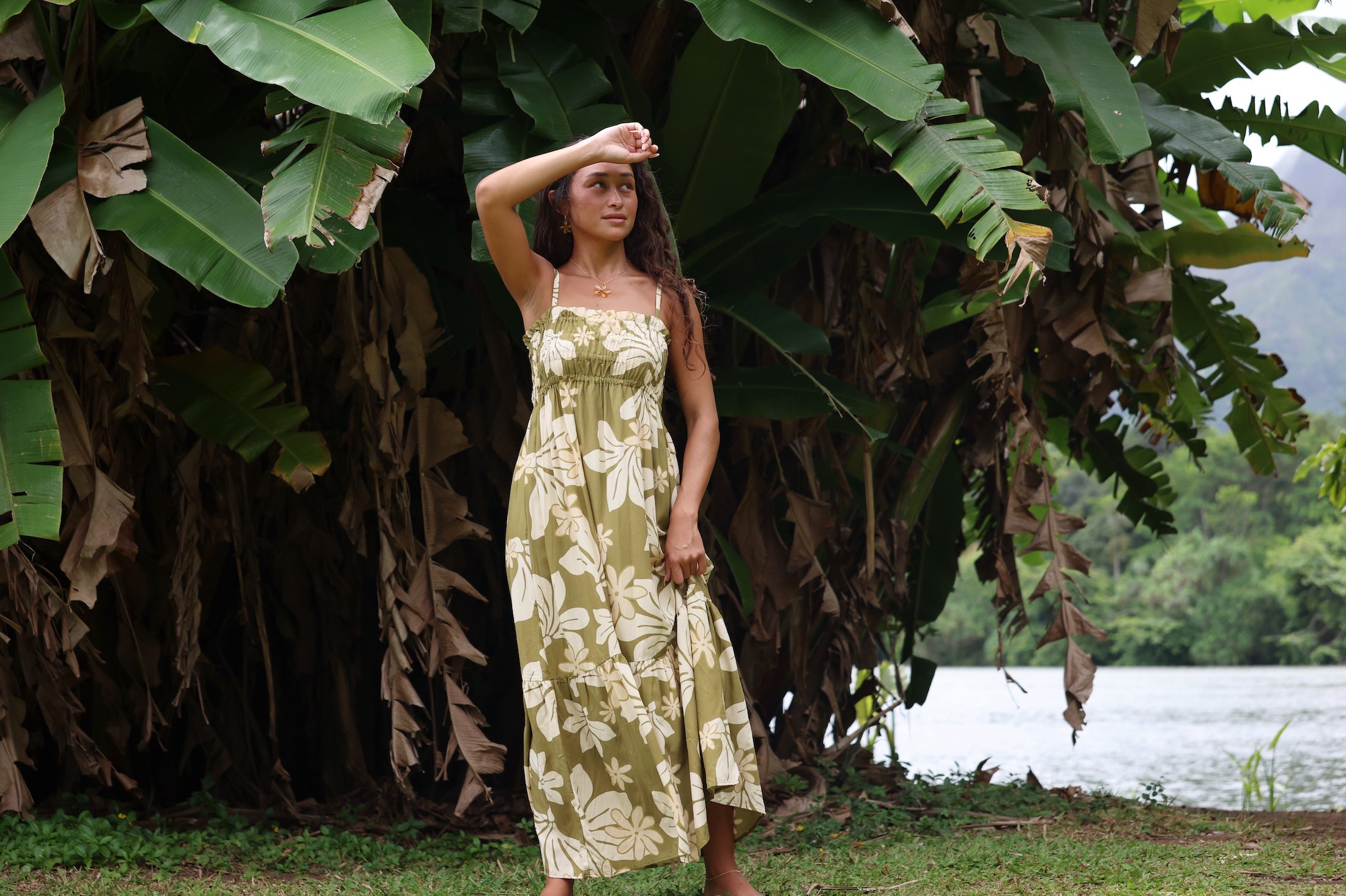 woman with brown hair wearing a maxi flowy dress in a green color with naupaka pattern throughout.