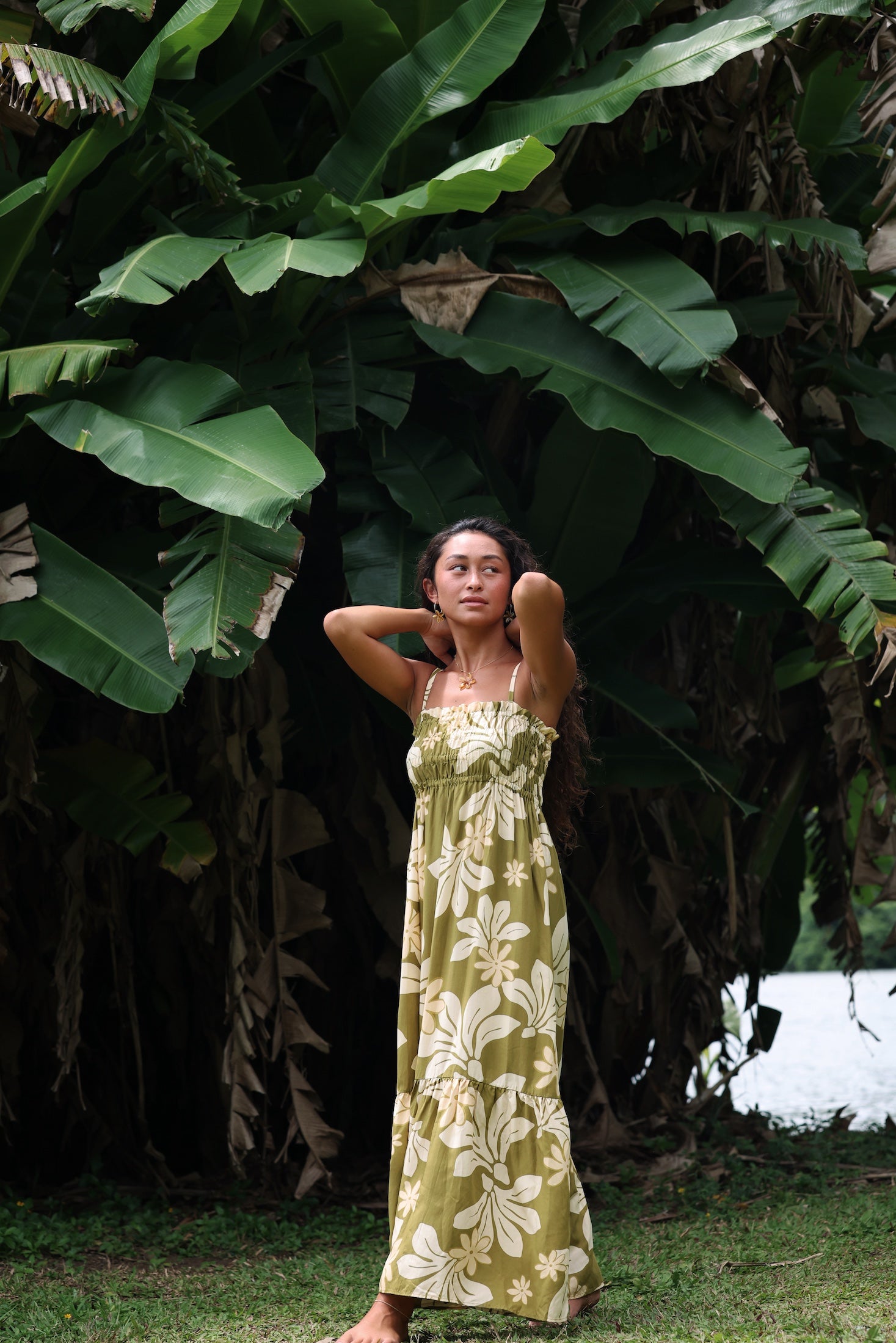 woman with brown hair wearing a maxi flowy dress in a green color with naupaka pattern throughout.
