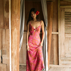A woman with dark hair wears a YIREH full length dress featuring a knotted, sweetheart neckline. It is the Marina Dress in the Garden 'Awapuhi print.
