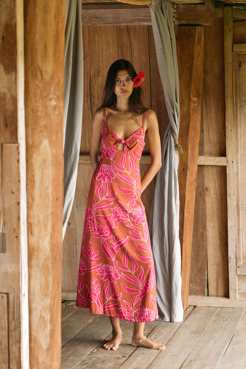 A woman with dark hair wears a YIREH full length dress featuring a knotted, sweetheart neckline. It is the Marina Dress in the Garden 'Awapuhi print.