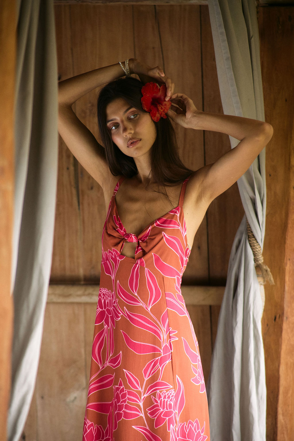 A woman with dark hair wears a YIREH full length dress featuring a knotted, sweetheart neckline. It is the Marina Dress in the Garden 'Awapuhi print.
