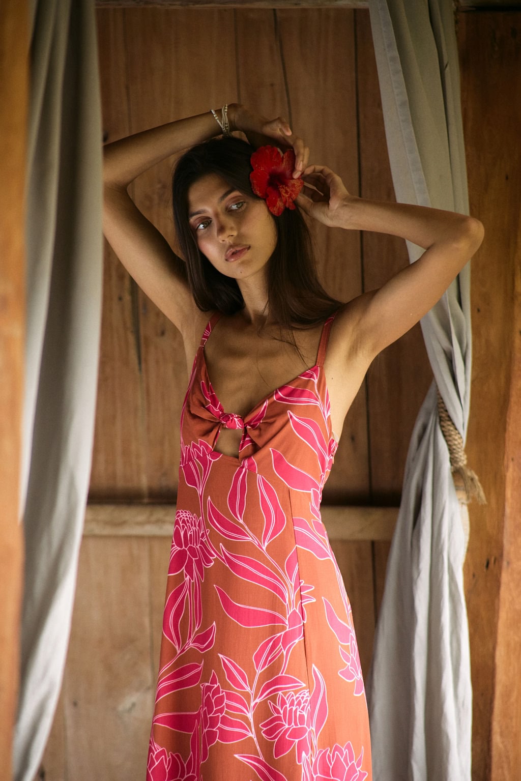 A woman with dark hair wears a YIREH full length dress featuring a knotted, sweetheart neckline. It is the Marina Dress in the Garden 'Awapuhi print.