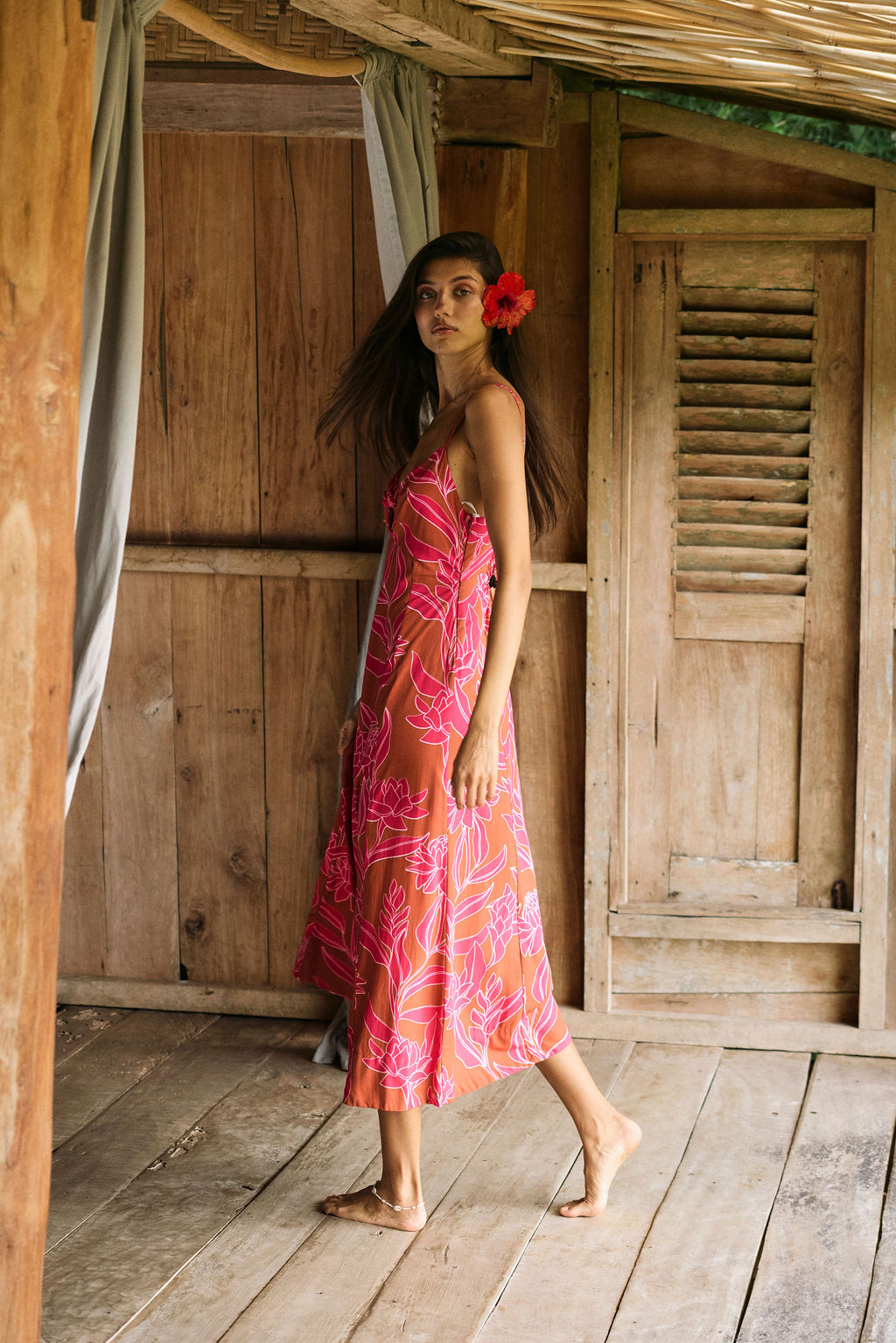 A woman with dark hair wears a YIREH full length dress featuring a knotted, sweetheart neckline. It is the Marina Dress in the Garden 'Awapuhi print.