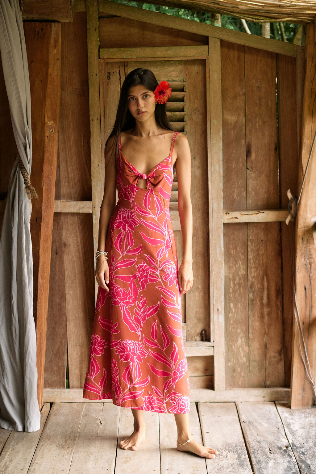 A woman with dark hair wears a YIREH full length dress featuring a knotted, sweetheart neckline. It is the Marina Dress in the Garden 'Awapuhi print.