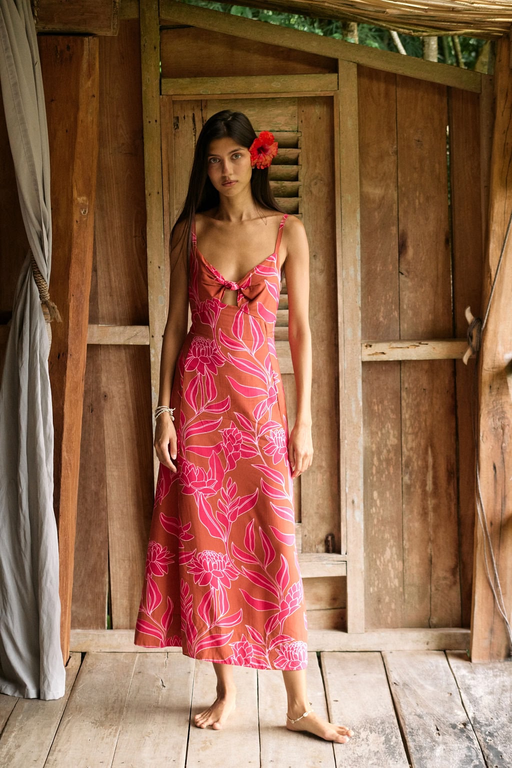 A woman with dark hair wears a YIREH full length dress featuring a knotted, sweetheart neckline. It is the Marina Dress in the Garden 'Awapuhi print.