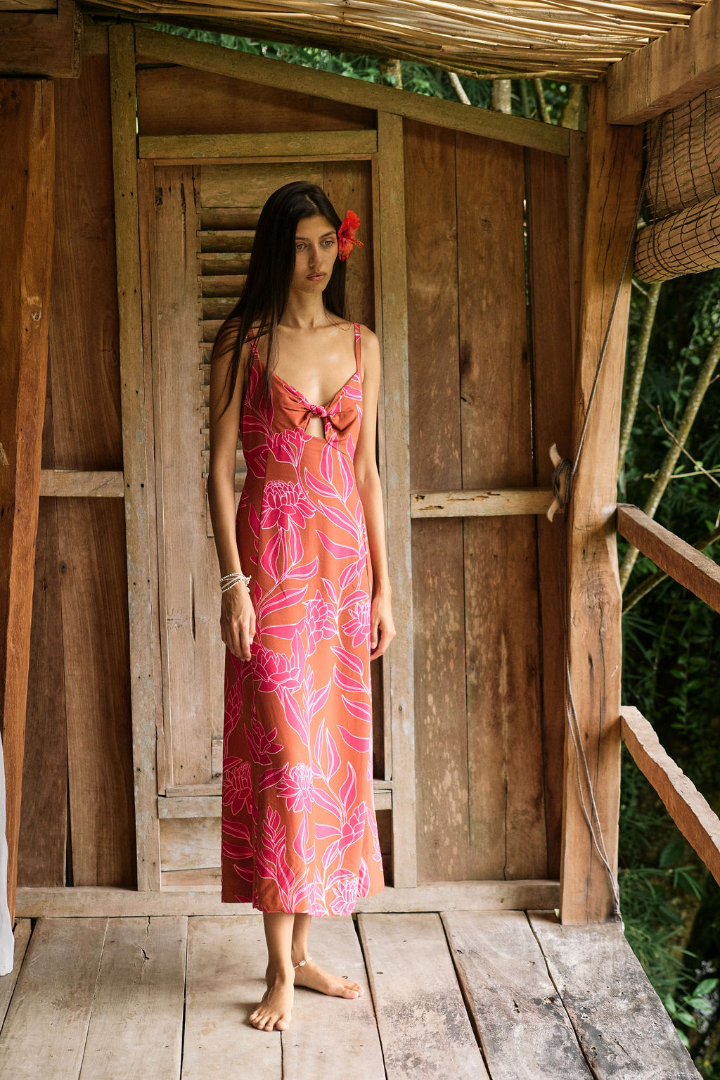 A woman with dark hair wears a YIREH full length dress featuring a knotted, sweetheart neckline. It is the Marina Dress in the Garden 'Awapuhi print.