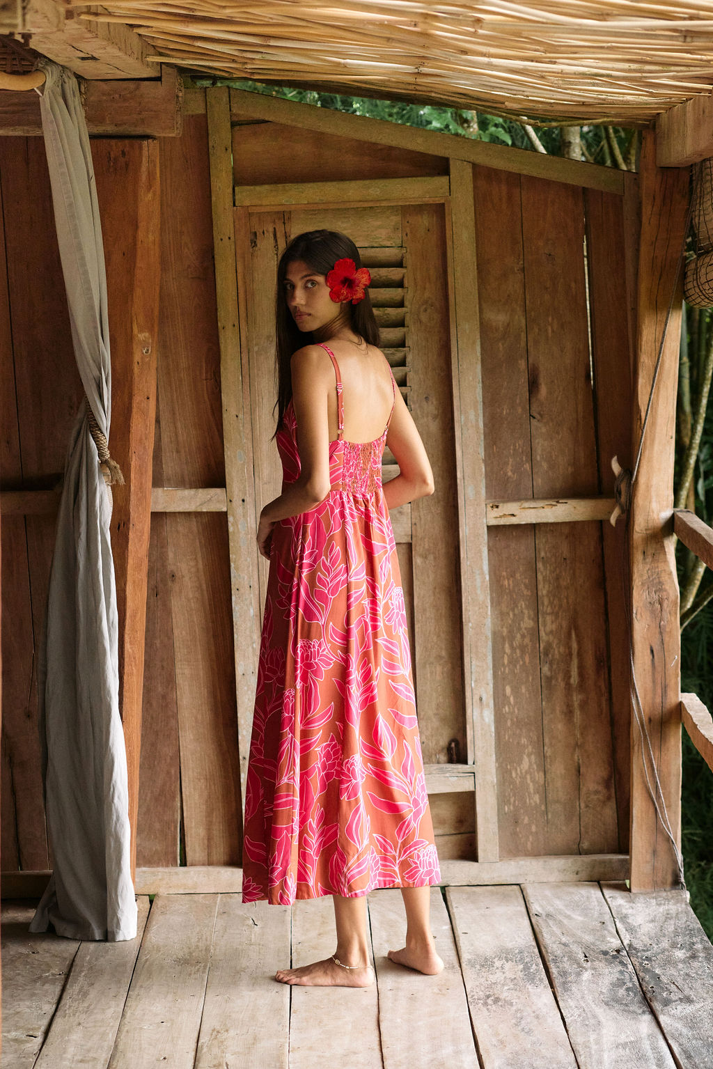 A woman with dark hair wears a YIREH full length dress featuring a knotted, sweetheart neckline. It is the Marina Dress in the Garden 'Awapuhi print.