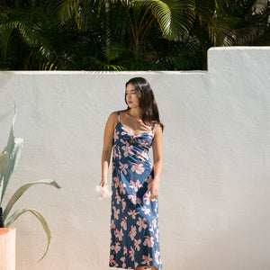 woman with black hair wearing a maxi dress with knot cutout neckline in a navy and pink hibiscus print.