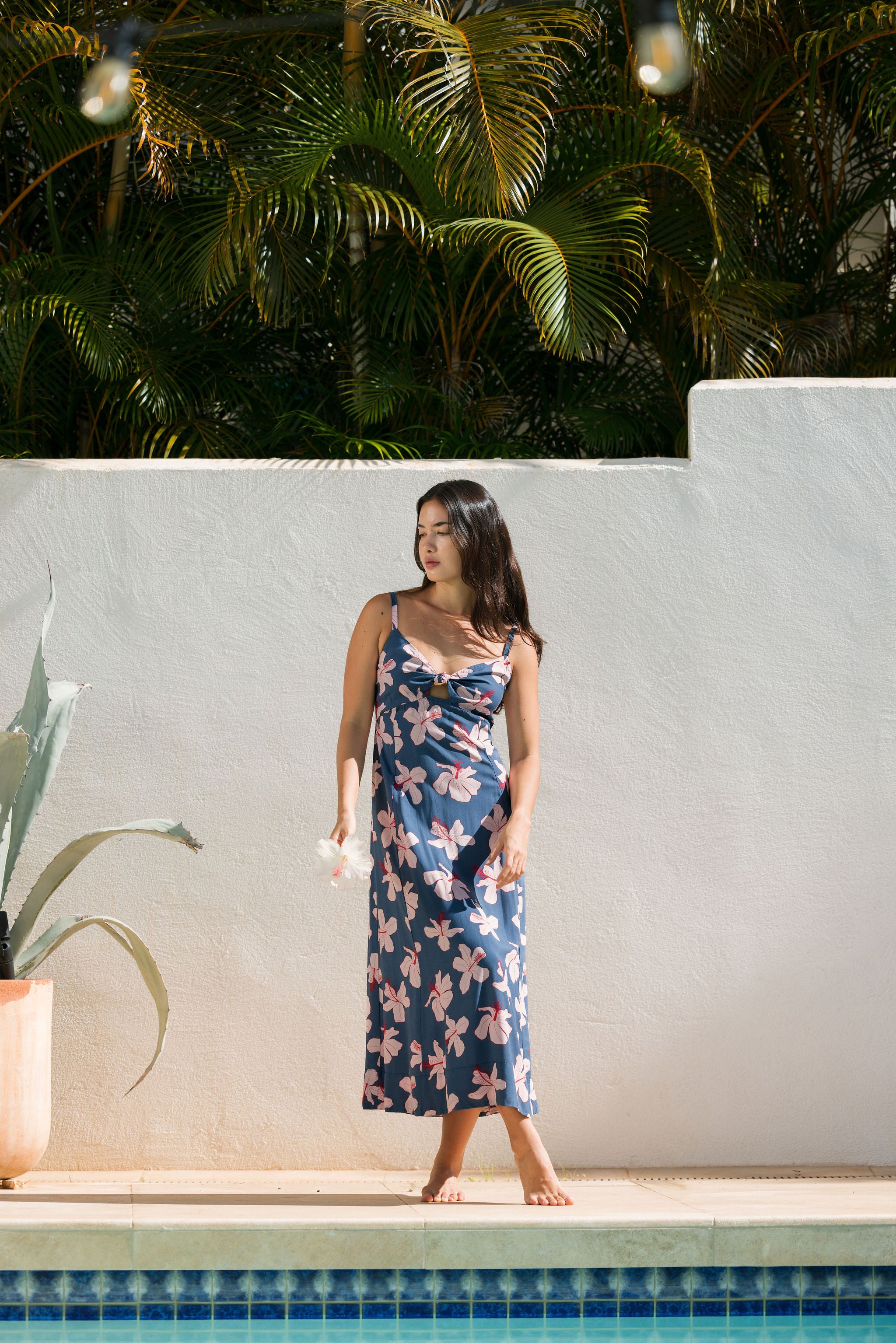 woman with black hair wearing a maxi dress with knot cutout neckline in a navy and pink hibiscus print.