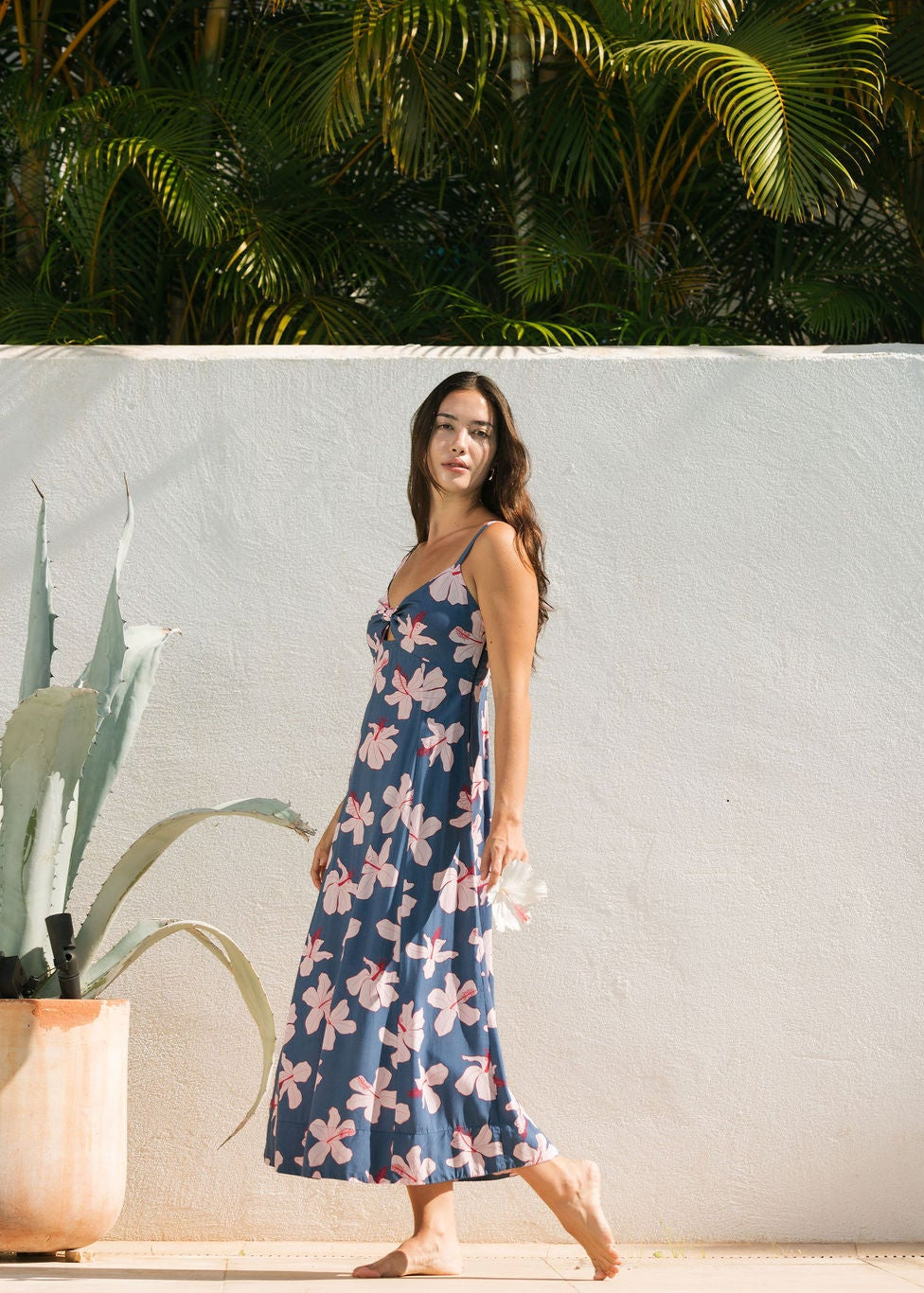 woman with black hair wearing a maxi dress with knot cutout neckline in a navy and pink hibiscus print.