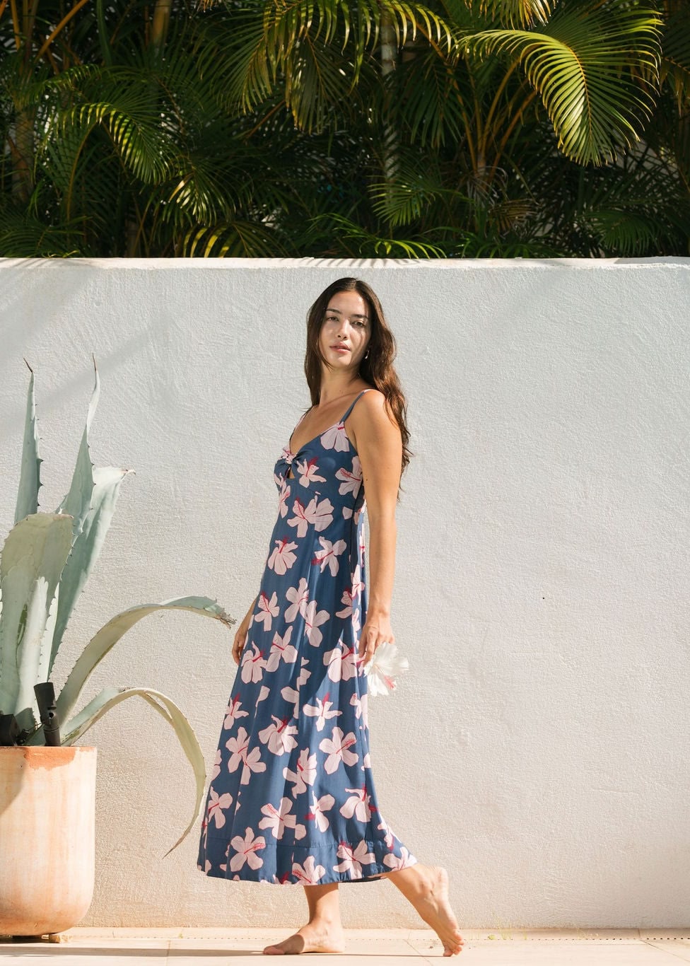 woman with black hair wearing a maxi dress with knot cutout neckline in a navy and pink hibiscus print.