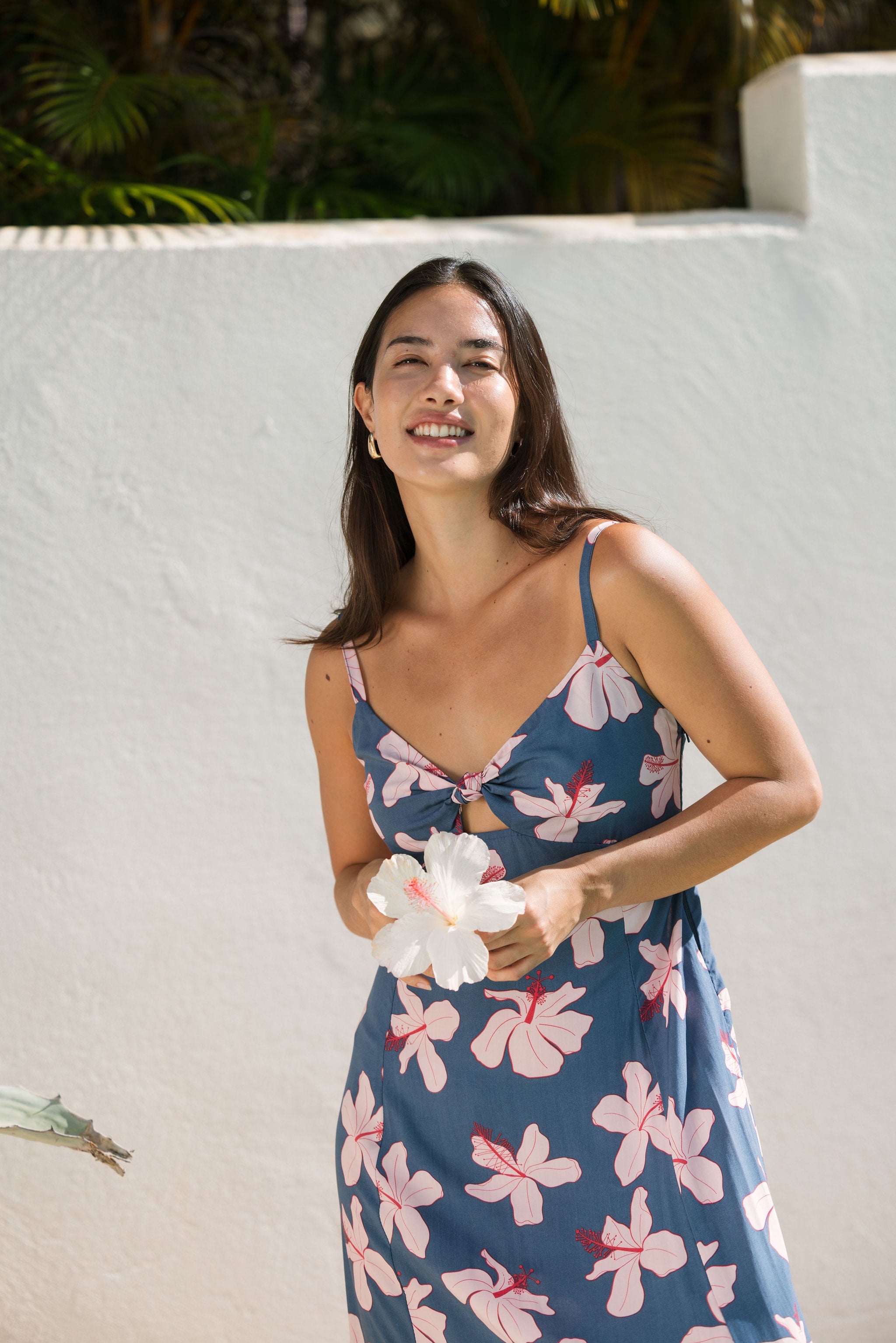 woman with black hair wearing a maxi dress with knot cutout neckline in a navy and pink hibiscus print.