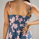 woman with black hair wearing a maxi dress with knot cutout neckline in a navy and pink hibiscus print.