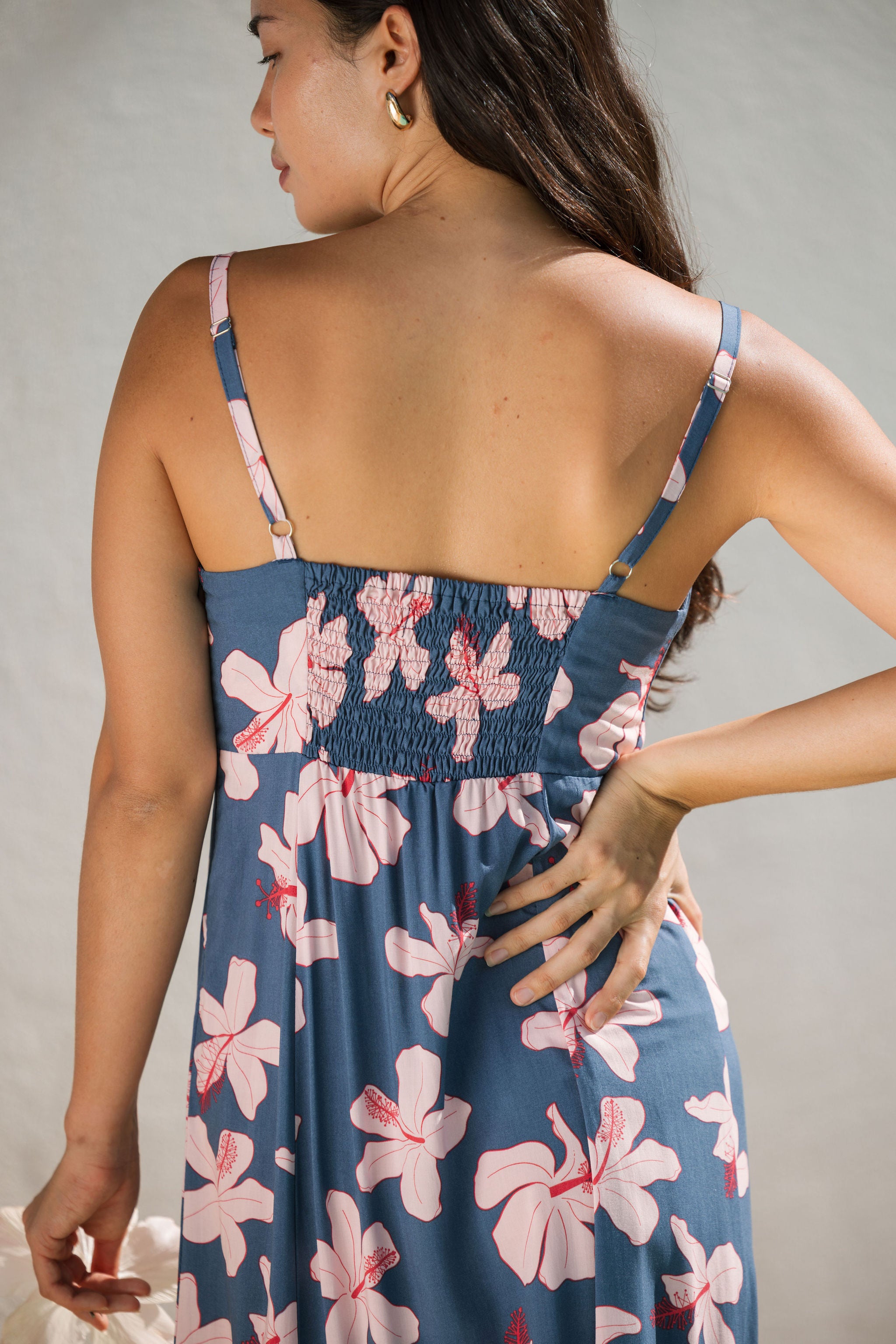 woman with black hair wearing a maxi dress with knot cutout neckline in a navy and pink hibiscus print.
