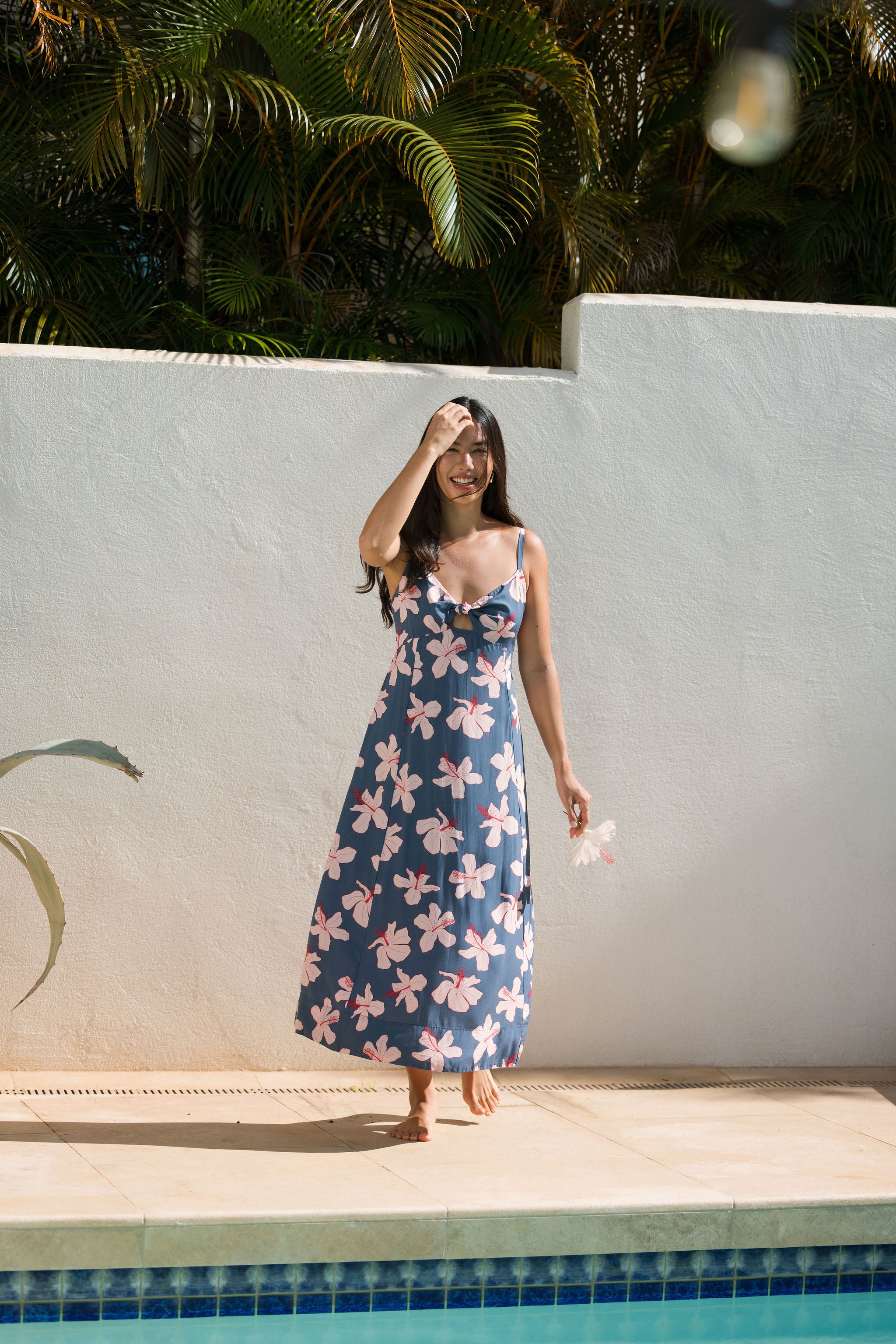 woman with black hair wearing a maxi dress with knot cutout neckline in a navy and pink hibiscus print.